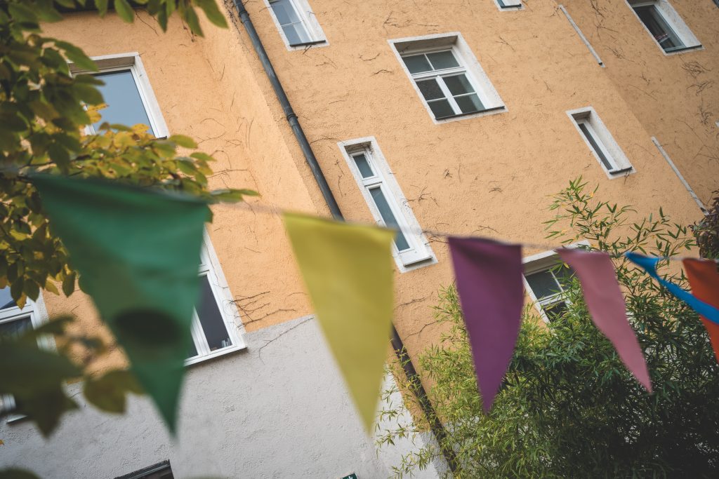 Bunte Wimpelkette vor der Hausfassade einer Kita, im Hintergrund Fenster und gr&uuml;ne Zweige