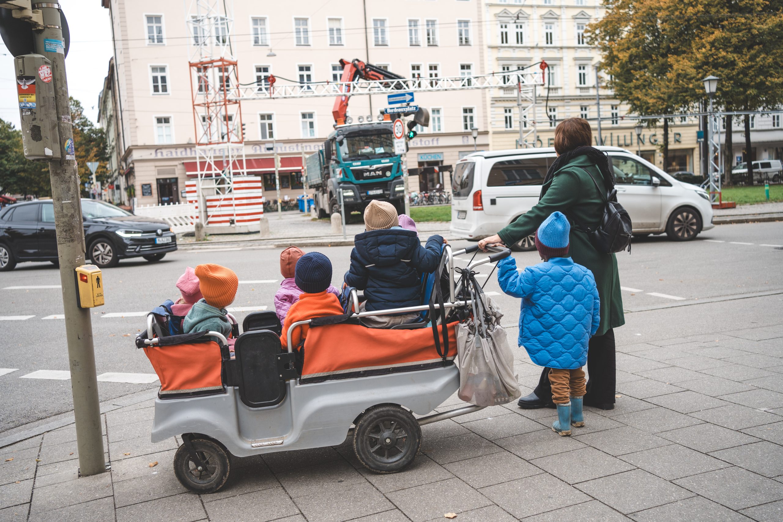 Erzieherin schiebt einen Krippenwagen mit Kindern &uuml;ber einen Gehweg in M&uuml;nchen