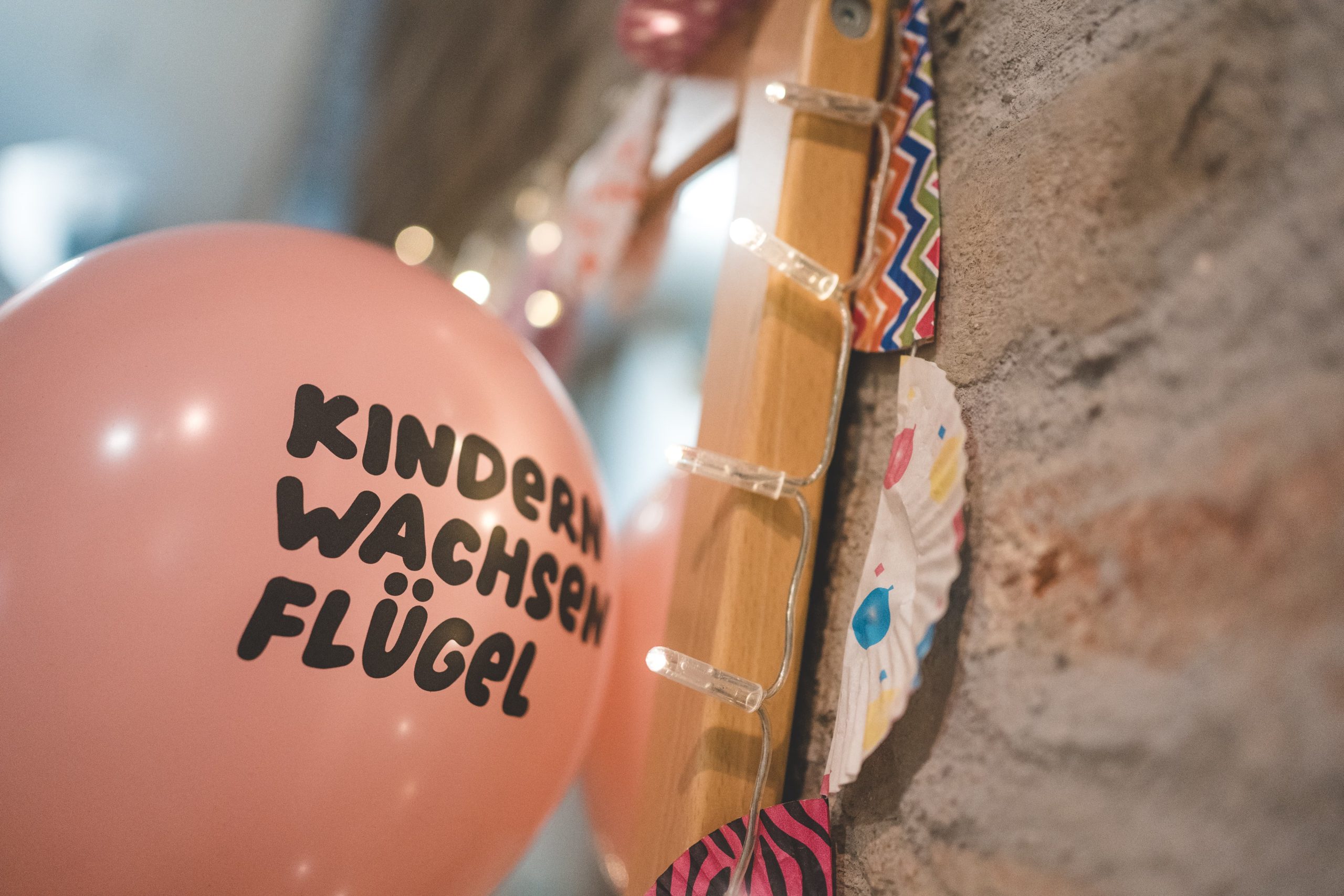 Rosa Luftballon mit der Aufschrift "Kindern wachsen Fl&uuml;gel" vor einer Gitarre und Deko an einer Steinwand