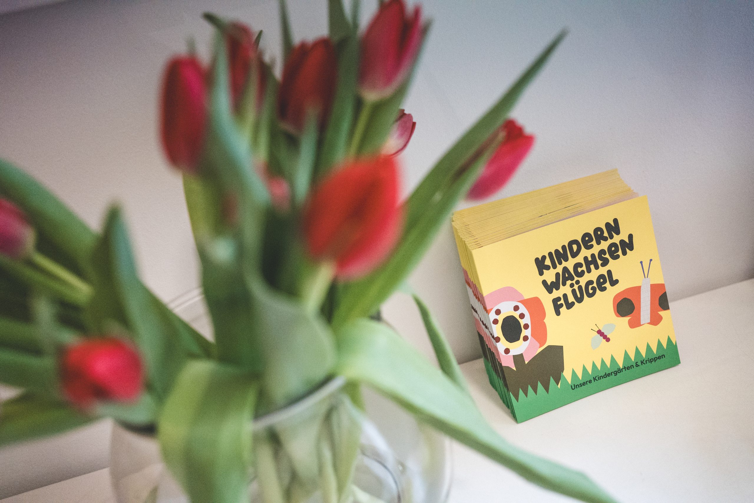 Rote Tulpen in einer Vase, daneben eine gelbe Verpackung mit dem Schriftzug Kindern wachsen Fl&uuml;gel